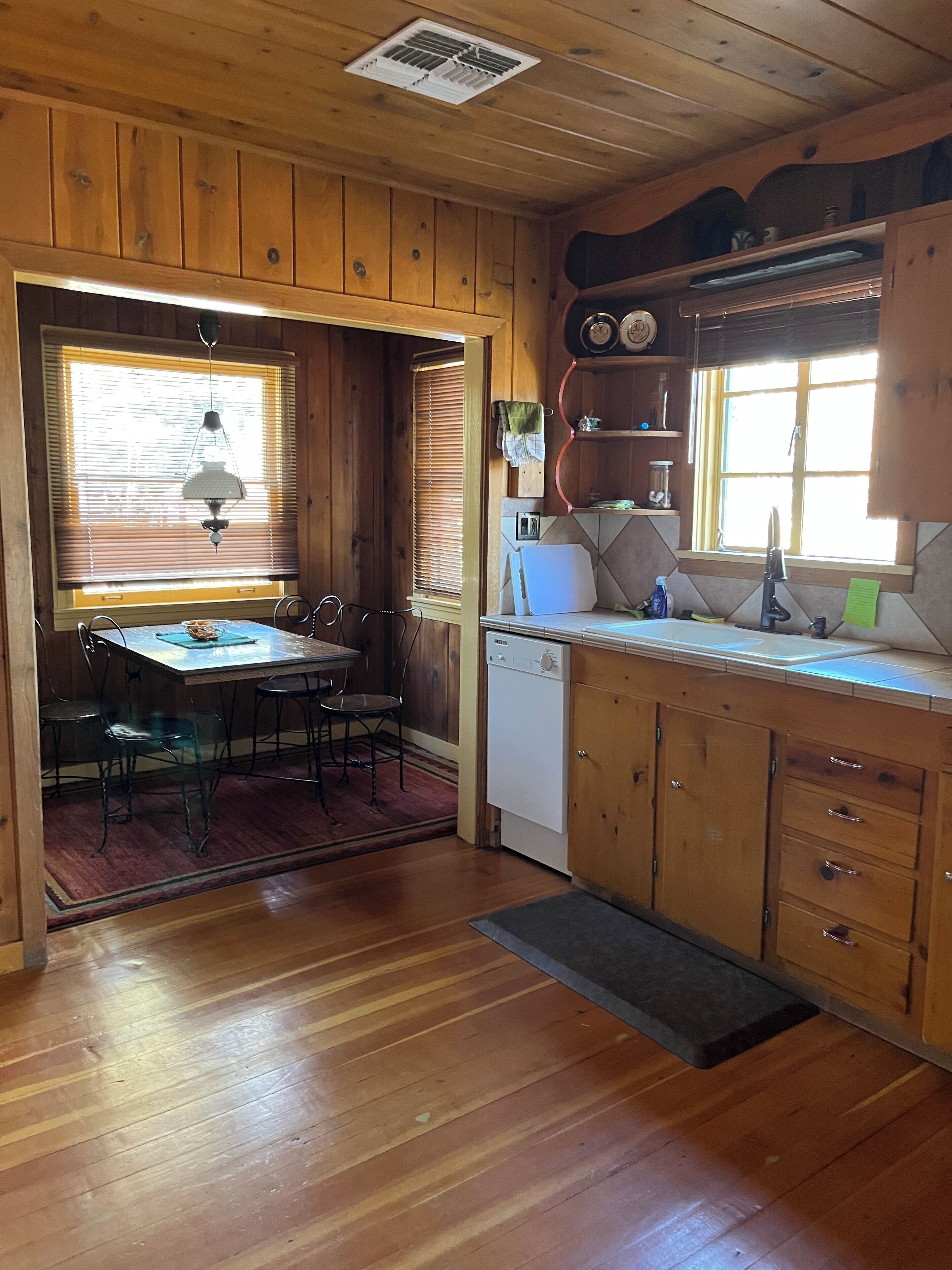 Interior de madera con una mesa de comedor, sillas, lavavajillas y una ventana con persianas.