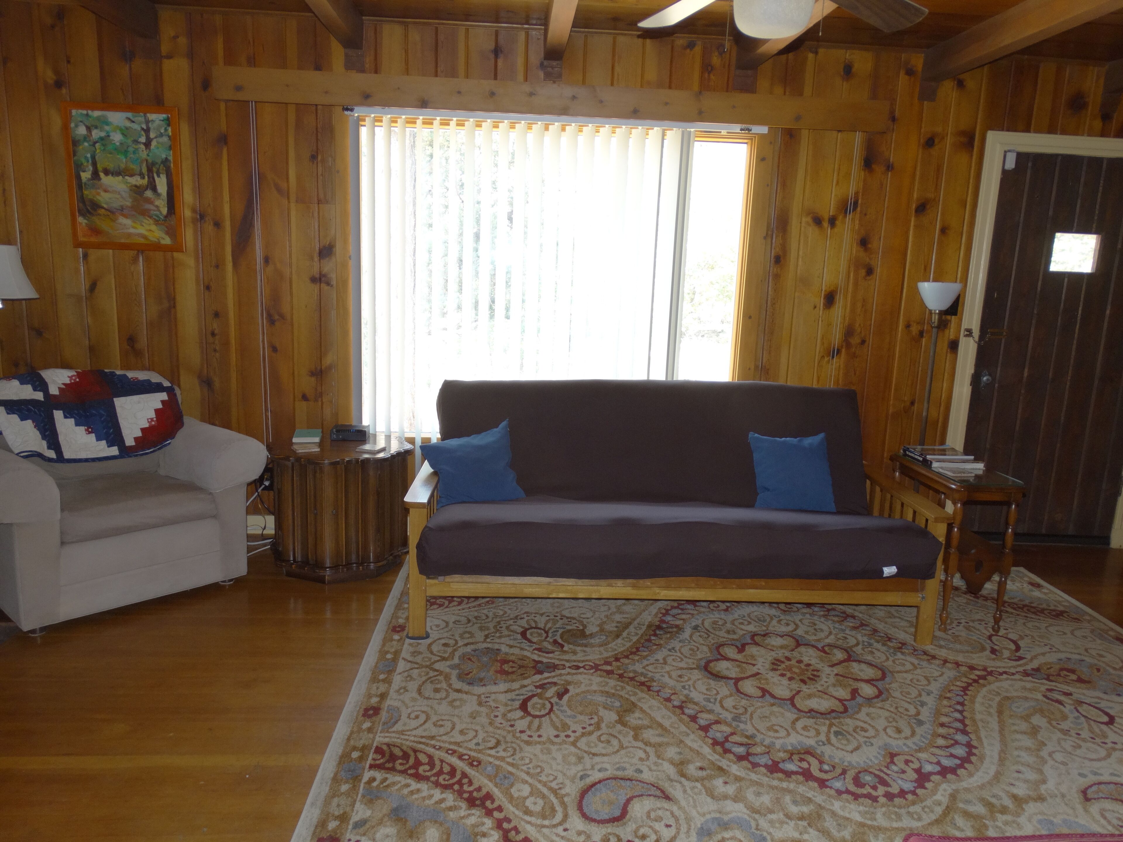 Una habitación acogedora con un sofá, una silla, un tapete estampado y paredes de madera.