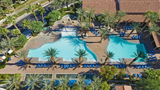 An aerial view of a resort with a large pool, palm trees, and blue lounge chairs. - Winter dates going fast! Beautifully renovated 3bd/3bth poolside, mountain views (La Quinta)