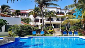 A swimming pool with blue water, surrounded by palm trees and lounge chairs. - Private Beachfront w/ Lanai-Pool-Tropical Gardens! (Akumal)