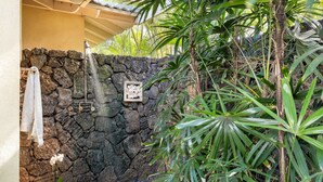 A stone wall with a shower, a towel hanging on the wall, and a potted plant.
