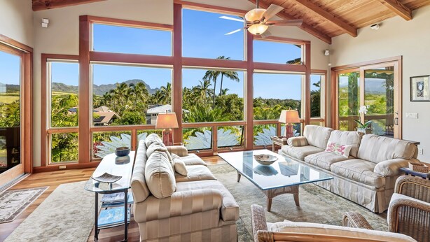 A spacious living room with large windows, a ceiling fan, and a view of palm trees and mountains.