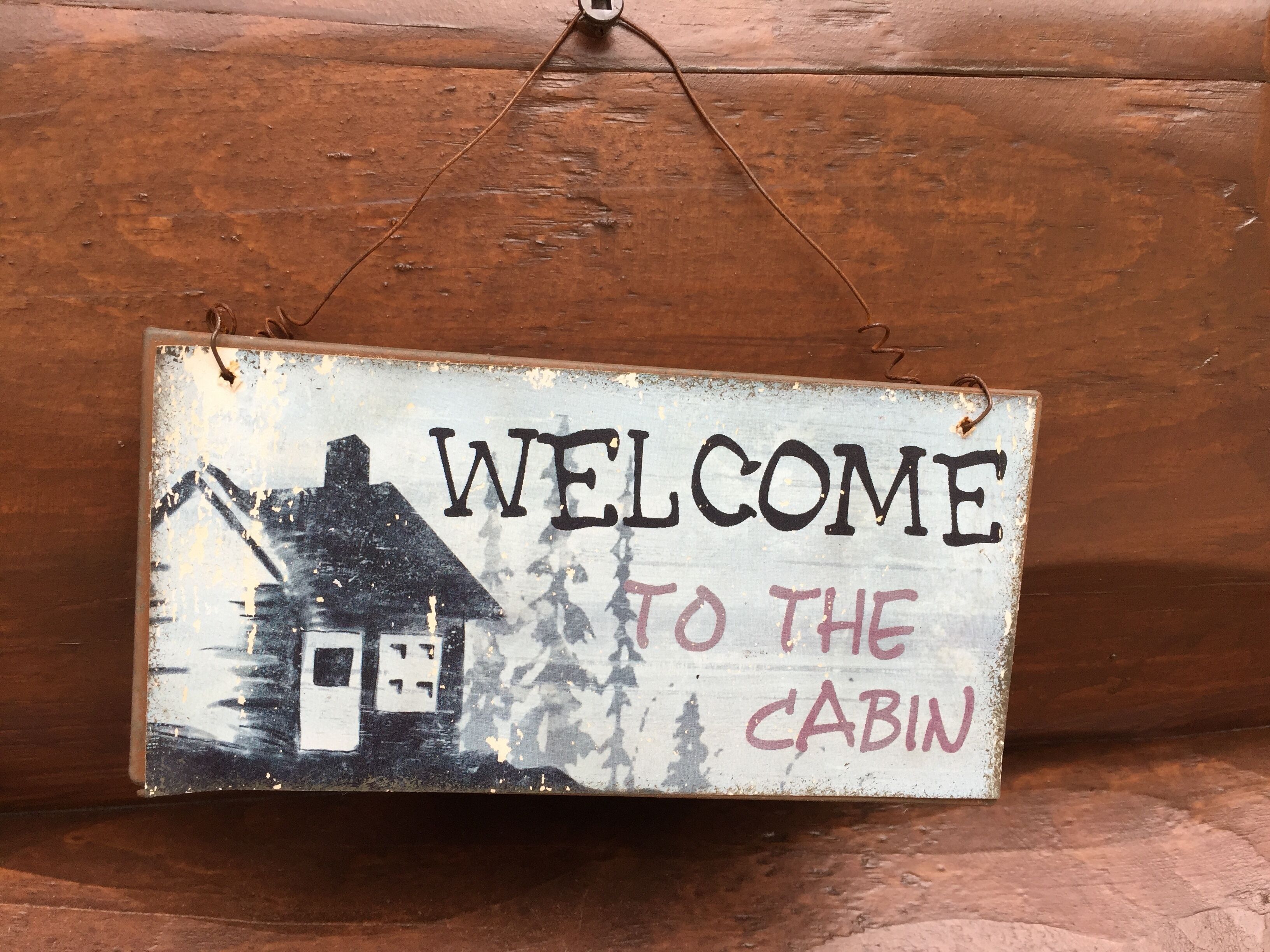 A rustic welcome sign with a cabin illustration and the text "WELCOME TO THE CABIN".