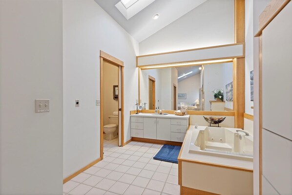 A modern bathroom with a skylight, a large mirror, a bathtub, and a toilet.