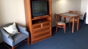 Ett rum med ett TV-bord i trä, en blå fåtölj, ett matbord i trä med stolar och en taklampa.