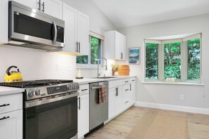 A modern kitchen with stainless steel appliances, white cabinetry, and a view of greenery through the windows.