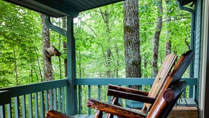 A wooden rocking chair on a porch with a view of a forest.