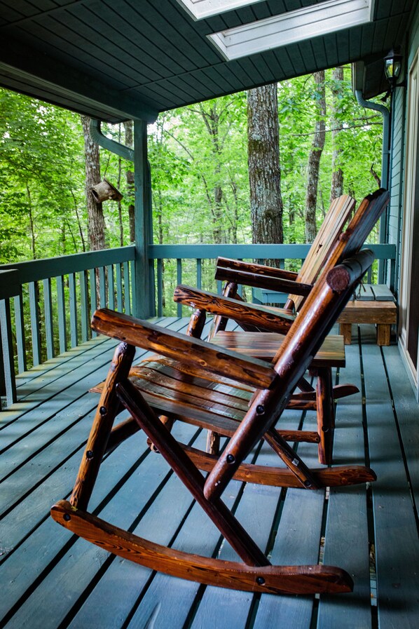 A wooden rocking chair on a porch with a view of a forest.