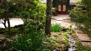 Un jardin avec un petit ruisseau, un banc en bois et une porte rouge.