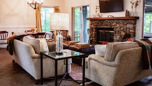 Un salon chaleureux avec une cheminée en pierre, des fauteuils confortables et un téléviseur fixé au mur.