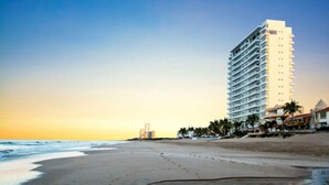 A beachfront hotel with multiple floors, a beach in the foreground, and palm trees along the shore. - Stunning Oceanfront Pearl Tower Condo - Pool, Gym &  Sunsets - 3 beds/4baths (Mazatlán)