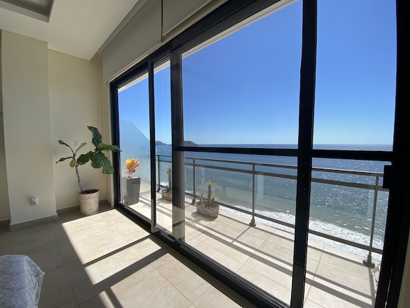 A balcony with a view of the sea, a potted plant, and a tiled floor.