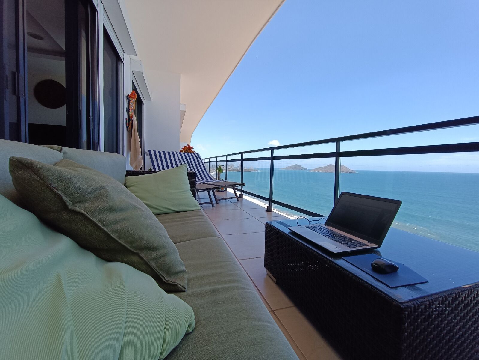 Ein Balkon mit einer Couch, einem Laptop und Blick auf das Meer.