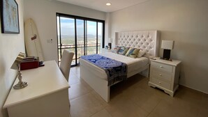 A bedroom with a bed, a desk, a chair, a nightstand, and a surfboard. - Stunning Oceanfront Pearl Tower Condo - Pool, Gym &  Sunsets - 3 beds/4baths (Mazatlán)
