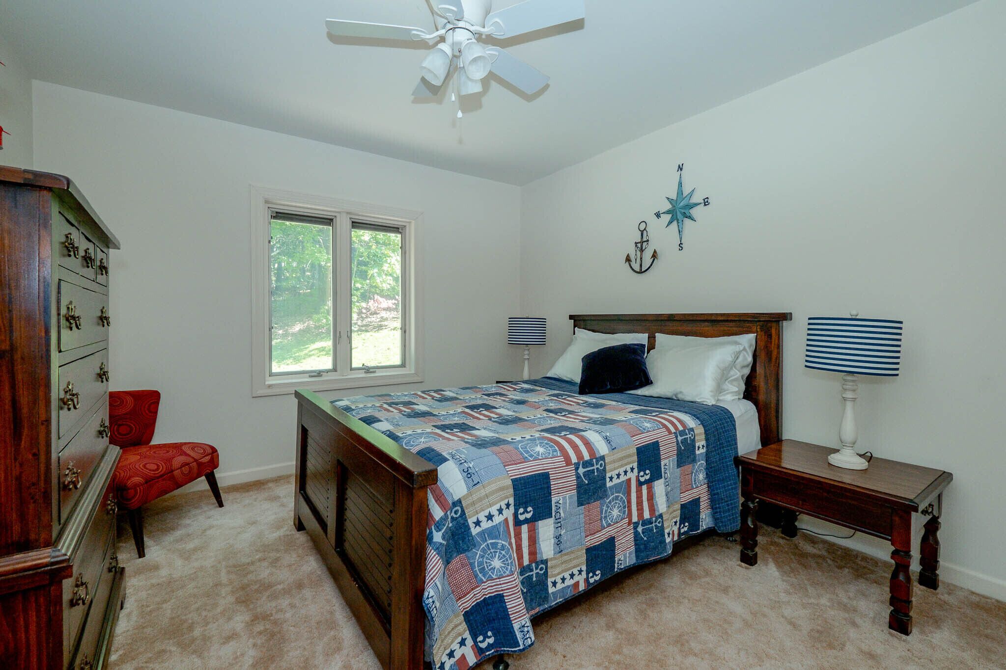A bedroom with a wooden bed, a dresser, a chair, a window, and a ceiling fan.