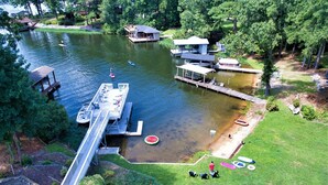 A lakeside property with a dock, a floating house, and a grassy area with outdoor seating. - 3,500 sq ft MAIN LAKE - deep water, boat house, hot tub & beach! (Henrico)