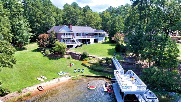 A lakeside property with a dock, a house, and a grassy area with boats. - 3,500 sq ft MAIN LAKE - deep water, boat house, hot tub & beach! (Henrico)