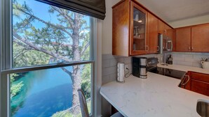 Cozinha com armários de madeira, bancada de mármore e vista para uma árvore e para a água lá fora.