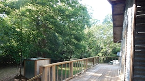 A wooden deck with a railing, surrounded by trees. - Camp House on Red Creek - Uncle Ralph’s Cabin Rentals - PRIVATE BEACH (Perkinston)