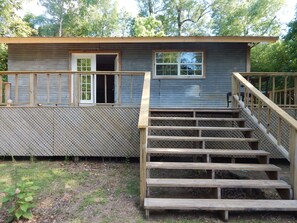 A wooden cabin with a small porch and a set of wooden stairs leading to a door.