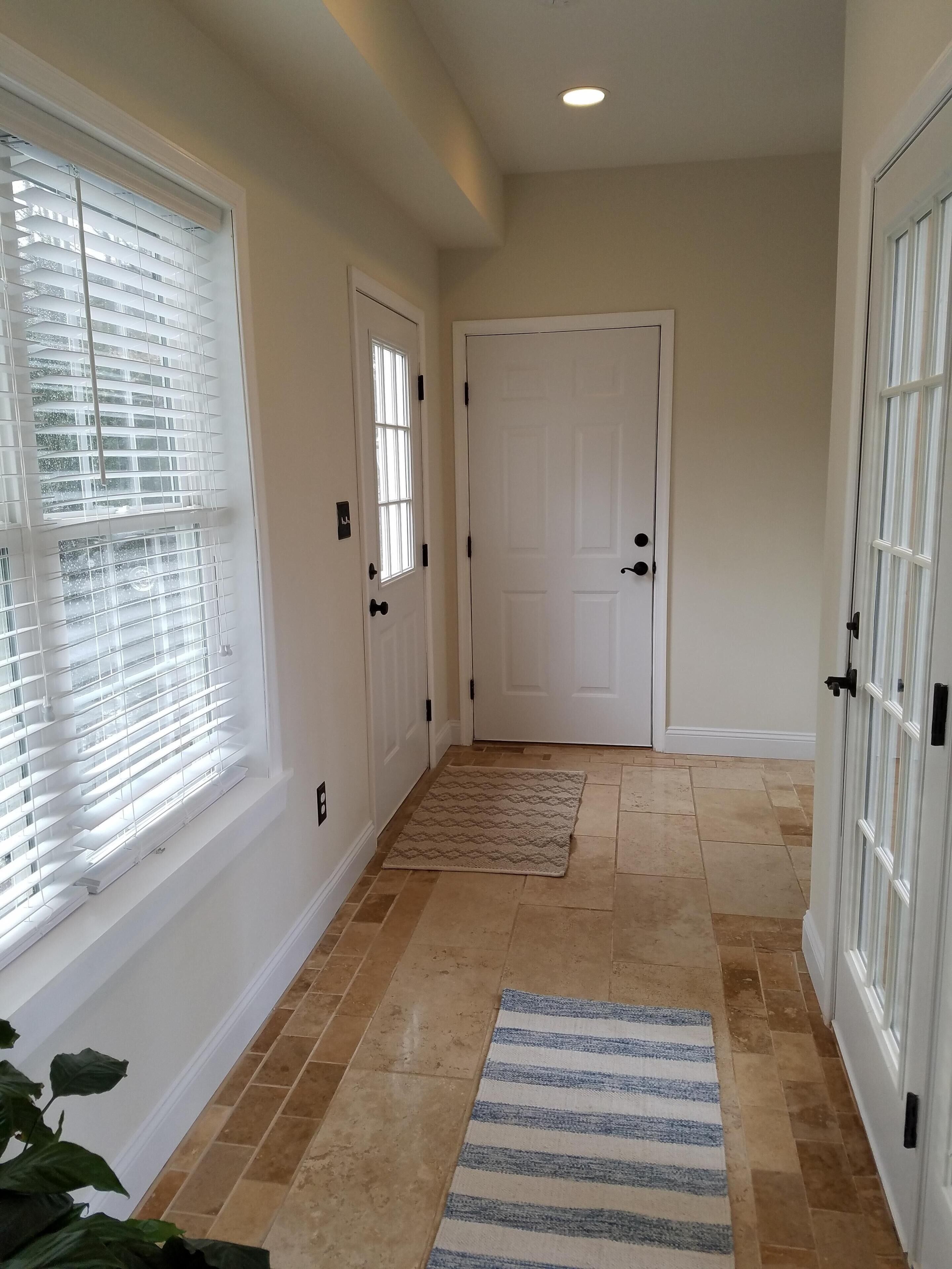 A hallway with two white doors, beige tiled flooring, and a striped rug.