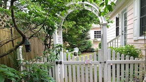 En indgang med låge, et skilt der siger 'CLOSE GATE', et træhegn og en stensti, der fører til et hus med veranda.