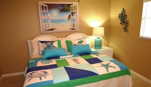 A bed with a quilt featuring sea creatures, a white headboard, and a decorative wall piece.