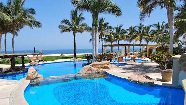 Un área de piscina con palmeras, sillas de descanso y vistas al océano.