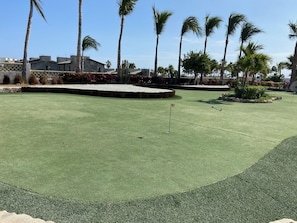 Un terrain de golf bien entretenu, doté d’un green d’entraînement, entouré de palmiers et d’un mur de pierre.