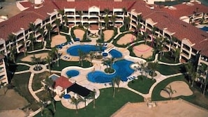 Un resort con varias piscinas, palmeras y un patio central.