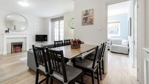 Un coin repas comprenant une table en bois, six chaises, une cheminée, un téléviseur et une horloge murale.