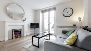 Un salon avec une cheminée, un téléviseur, un canapé et une horloge au mur.