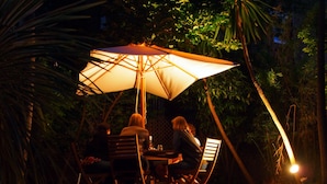 Un espace de restauration en plein air avec une table et des chaises placées sous un grand parasol, le tout entouré de verdure.