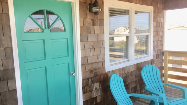 A turquoise door with a window above it, a wooden deck, and two turquoise Adirondack chairs. - Atlantic Oasis, less than 1 block to the beach! Private & Spacious, Full Kitchen (Nags Head)