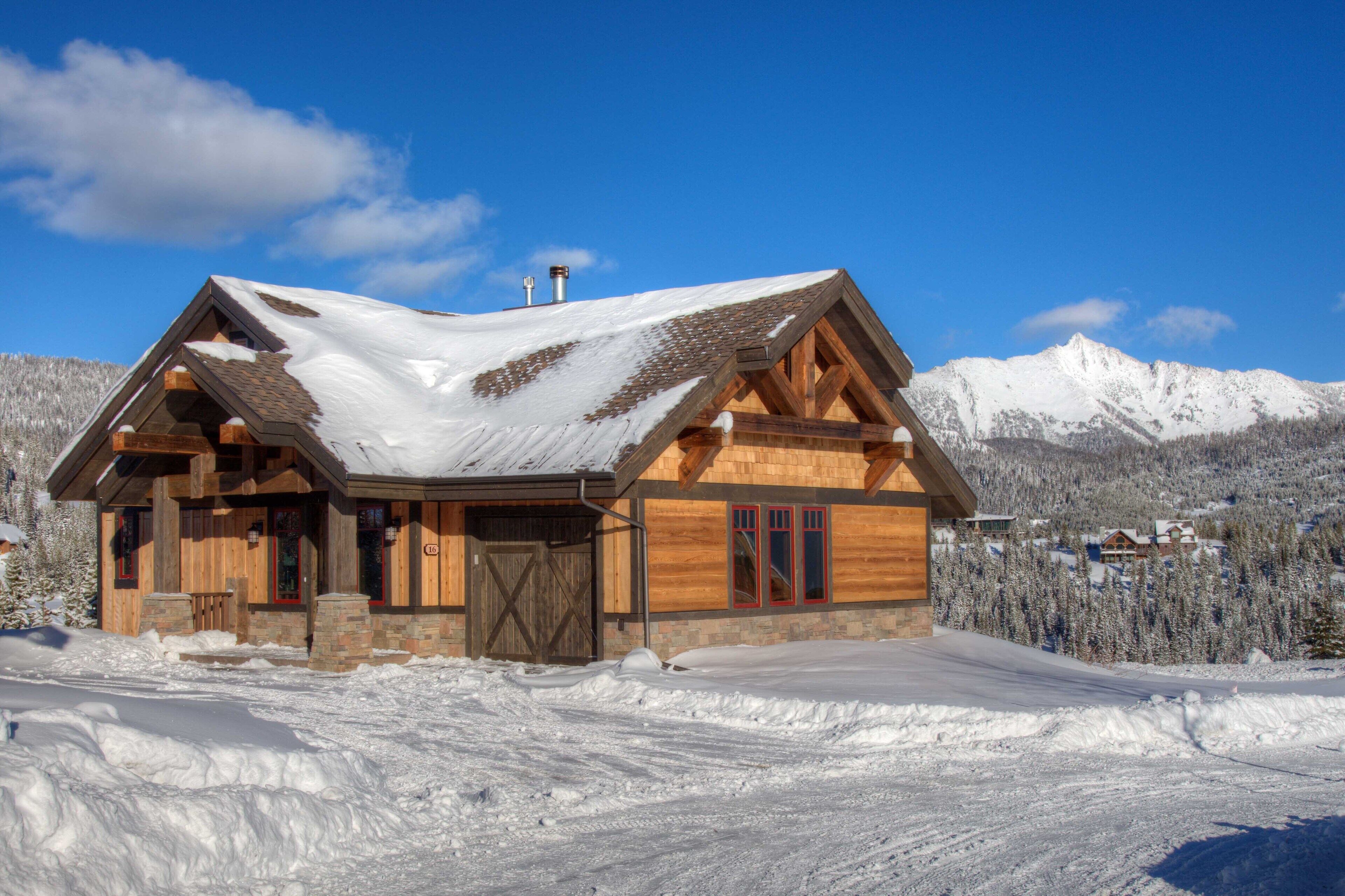 A wooden cabin with a sloped roof, a large wooden door, and a stone foundation.