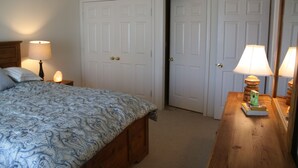 A bedroom with a bed, two doors, a nightstand with a lamp, and a dresser with a mirror.