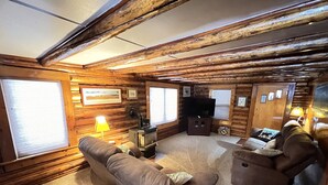 Interior acogedor de una cabaña con paredes de madera, un sofá, una silla, un televisor y una chimenea.