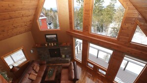 Ein gemütliches Blockhaus-Interieur mit Kamin aus Stein, Ledersofas und großen Fenstern mit weitreichender Aussicht.