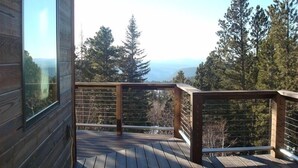 Eine Holzdielen-Terrasse mit Geländer, mit Blick auf bewaldetes Gelände und entfernte Berge.