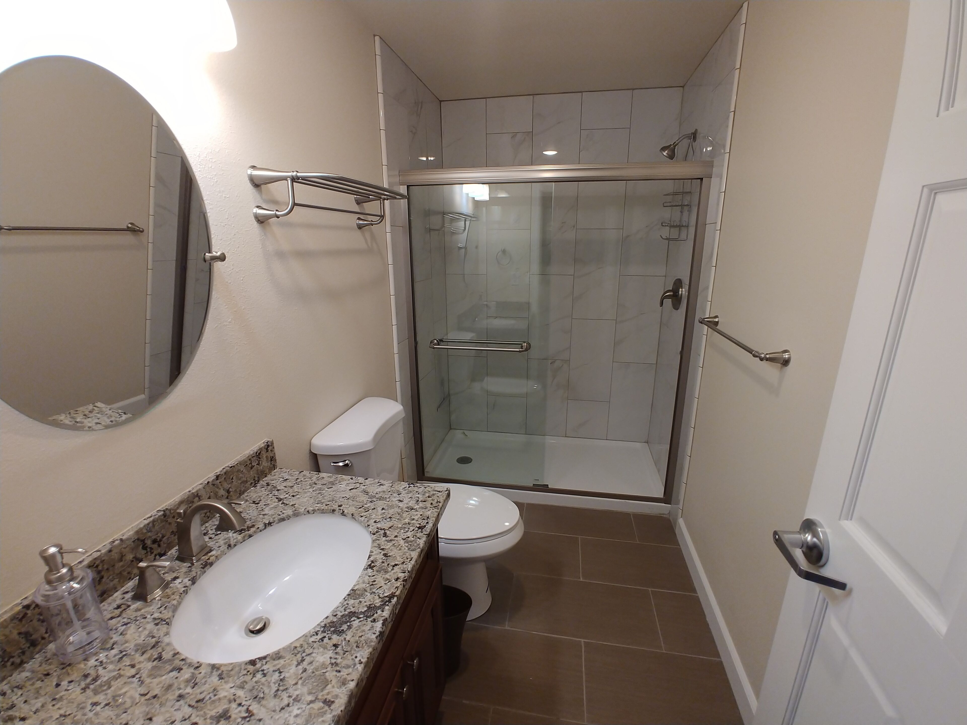 Un baño con encimera de granito, lavamanos, inodoro y cabina de ducha con paredes de vidrio.