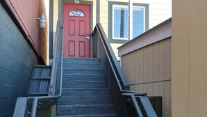 Una escalera de madera con barandales de metal que conduce a una puerta roja marcada con el número 214.
