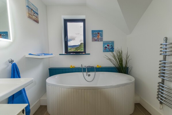A bathroom with a bathtub, a window, and a shelf with decorative items. - Explore the Ring of Kerry and Wild Atlantic Way (Cahirsiveen)