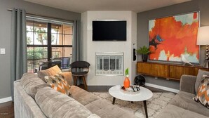 Een woonkamer met een grijze bank, een witte salontafel, een flatscreen televisie en een groot abstract schilderij.
