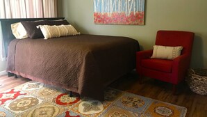Ein Schlafzimmer mit einem großen Bett, einem roten Sessel, einem bunten Teppich und einem Bild an der Wand.