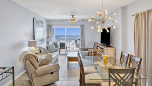 A spacious living area with a balcony, a dining table, and a modern chandelier. - Pet Friendly-Beach Front- West Corner Condo-2 Pools (Gulf Shores)