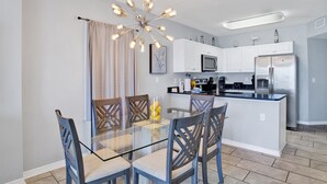 A modern kitchen with white cabinets, a stainless steel refrigerator, and a glass dining table with chairs. - Pet Friendly-Beach Front- West Corner Condo-2 Pools (Gulf Shores)