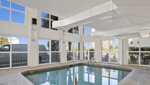 An indoor swimming pool with clear glass walls, a pool ladder, and a view of the outside. - Pet Friendly-Beach Front- West Corner Condo-2 Pools (Gulf Shores)
