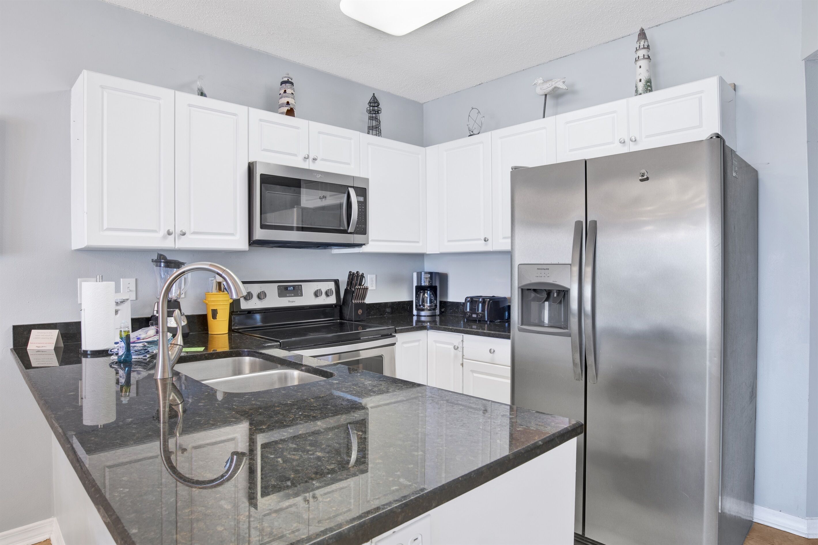 A modern kitchen with white cabinets, a stainless steel refrigerator, a microwave, and a sink.