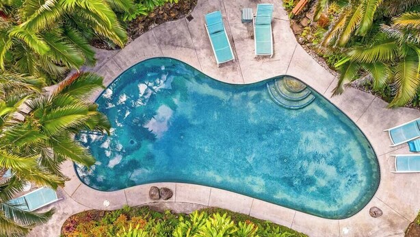 An aerial view of a swimming pool with lounge chairs and tropical plants. - Haleakala Cottage - private hot tub, pool access (Haiku)