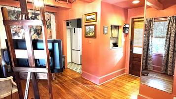 A room with wooden flooring, a television, a painting, and a mirror.